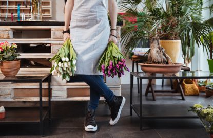 Closeup of young woman florist in apron and sneakers with two bouquets of tulips standing in flower shop