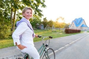 old people, leisure and lifestyle concept - Portrait of senior woman 60-65 years old on bicycle. Older lady riding city bike in european town. Smiling old female cycling with her bike in summer time